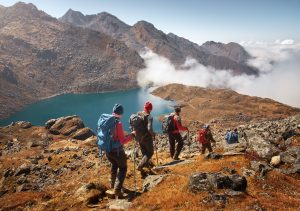 Group of tourists with backpacks descends down mountain trail to lake during a hike in the national park Lantang, Nepal.