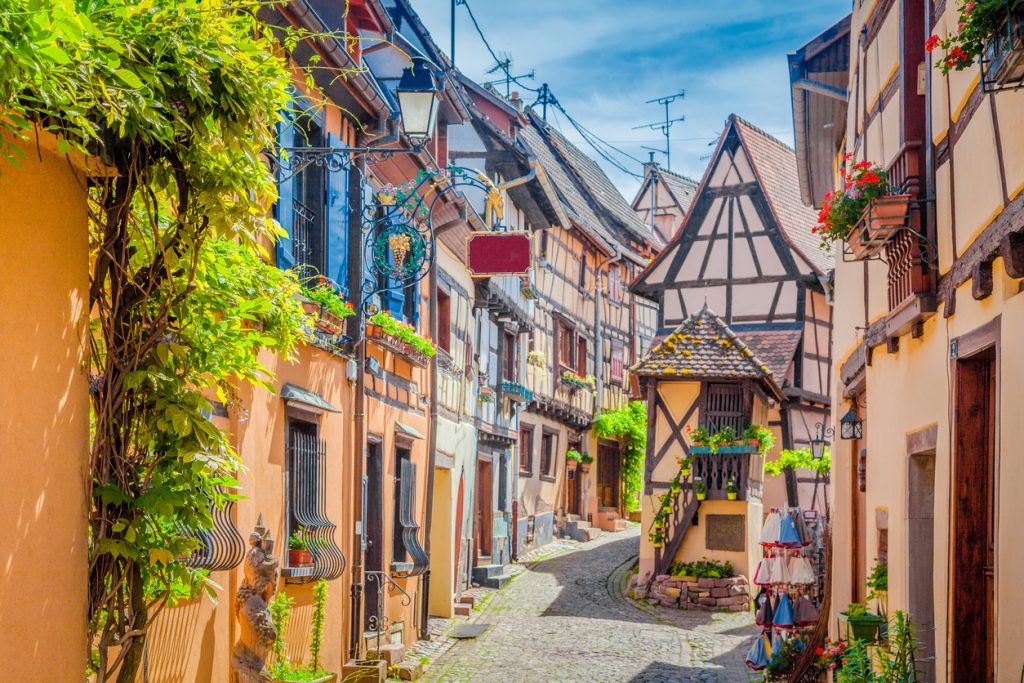 Charming street scene with colorful houses in the historic town of Eguisheim on a beautiful sunny day with blue sky and clouds in summer, Alsace, France