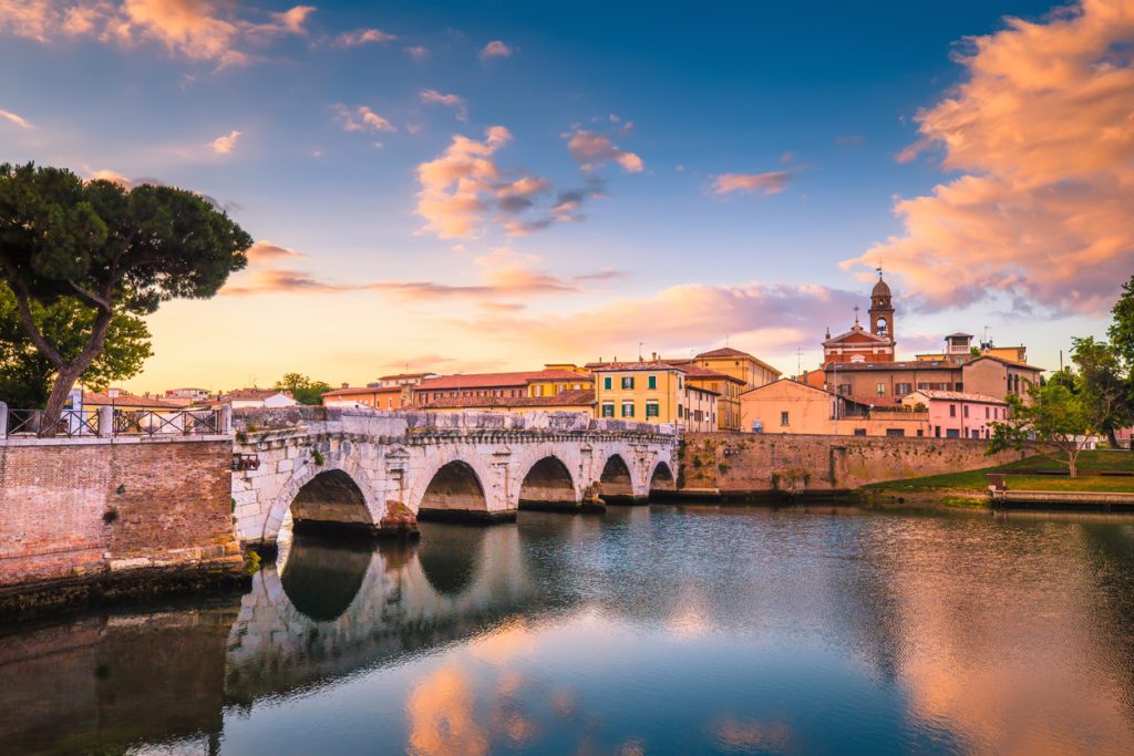 Rimini cityscape. Tiberius bridge famous sightseeing in Rimini at dawn. Summer sunrise in Rimini historic center.