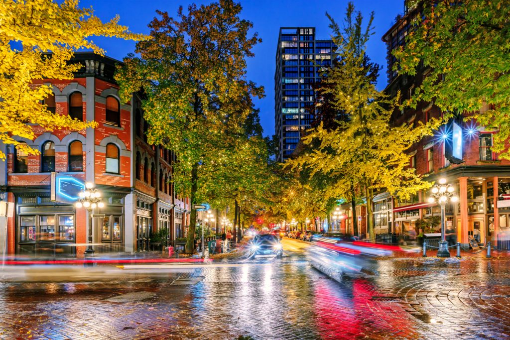 Night on the street in the old part of the big city with the lights of storefronts and shops, the blinding lights of car headlights and a paved roadway shimmering in neon lights after the last rain