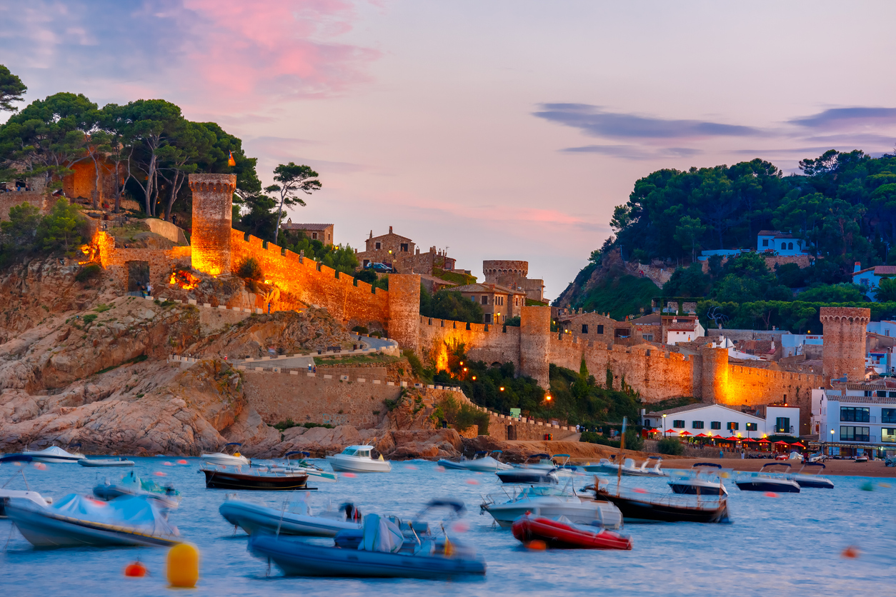 Fortress and fishing boats at Gran Platja beach and Badia de Tossa bay at sunset in Tossa de Mar on Costa Brava, Catalunya, Spain