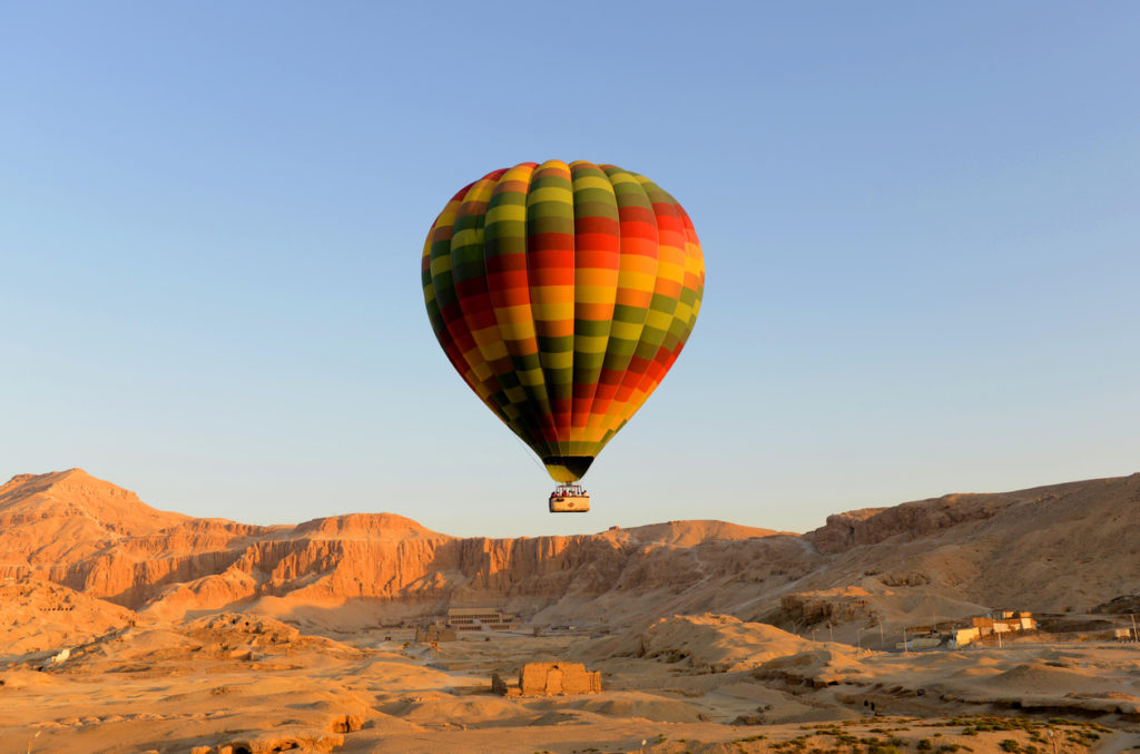 Hot air balloon lifting off in Luxor, Egypt with the temple of Hatshepsut in background