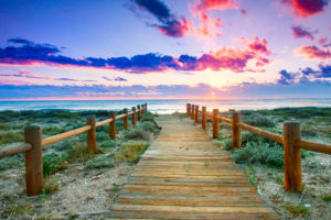 Wooden walkway through the grass to the beach under colourful sky