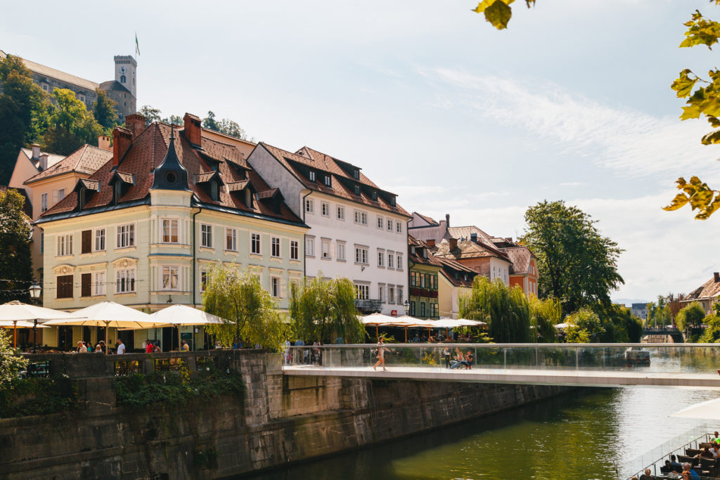 A beautiful view at river Ljubljanica, Cankarjevo Nabrezje, bridges and Ljubljana Castle tower, the tourist centre of Ljubljana, the capital of Slovenia. With people relaxing in cafes at the both banks of the river