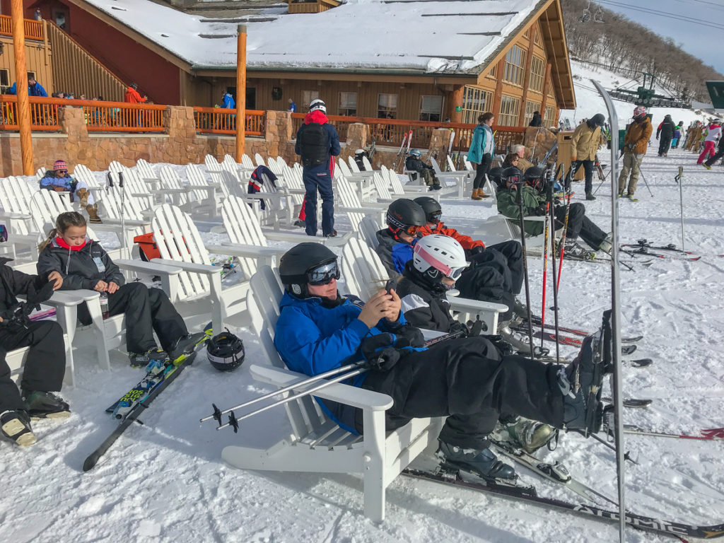 Skiers are sittting on chairs outside of Silver Lake lodge at Deer Valley resort.