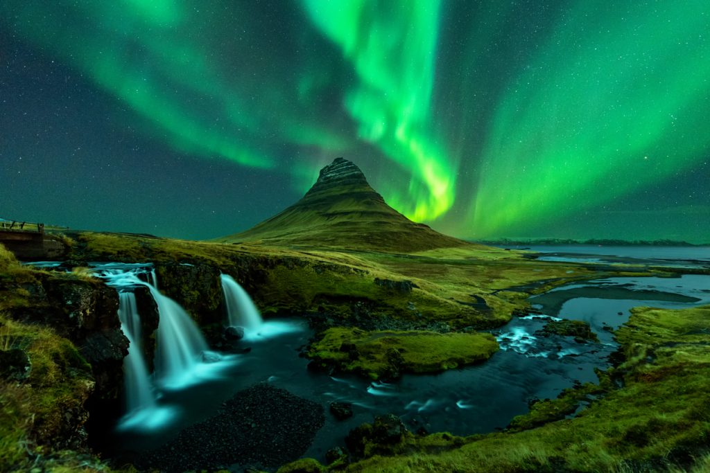 Northern lights appear over Mount Kirkjufell with kirkjufellfoss waterfall in Iceland.