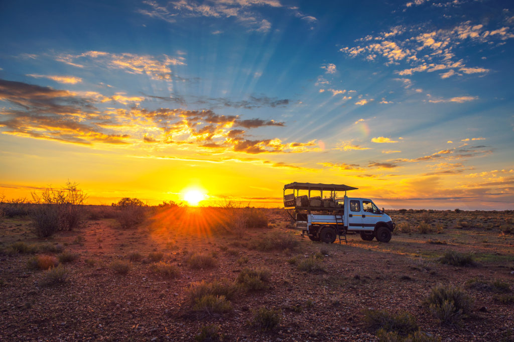 Safari vehicle stops in the Kalahari desert for a dramatic sunset