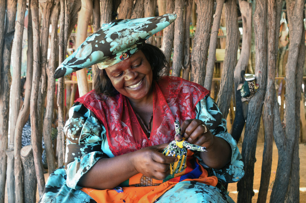 Herero woman , belonging to the Banto group wearing traditional clothing making a doll.