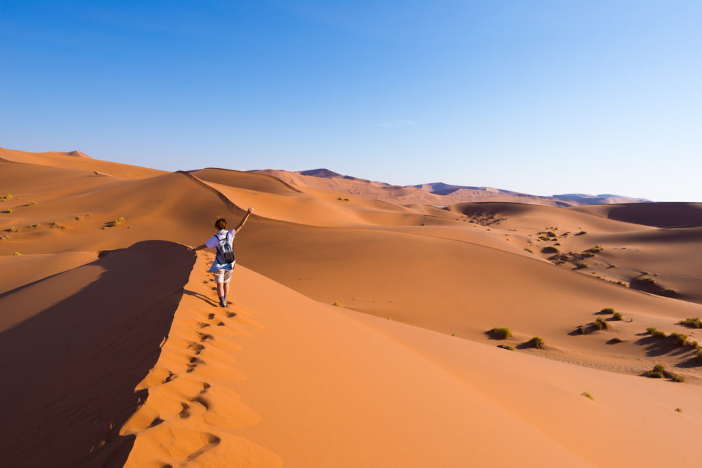 Tourist walking on the sand dunes of Sossusvlei, Namib desert, Namib Naukluft National Park, Nambia.