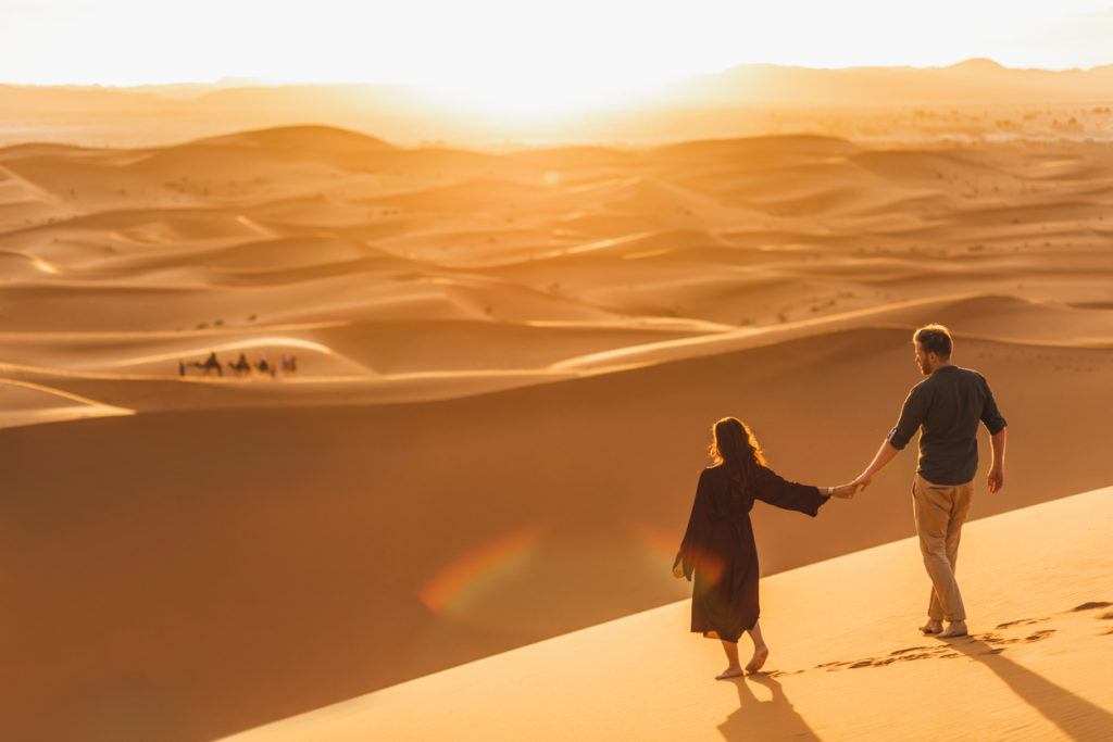 A couple walking in the Sahara desert at Sunset